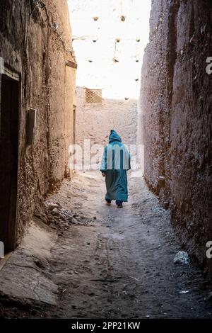 Silhouette eines Mannes in einer türkisfarbenen Djellaba, der durch die Gassen einer alten Kasbah geht. Stockfoto