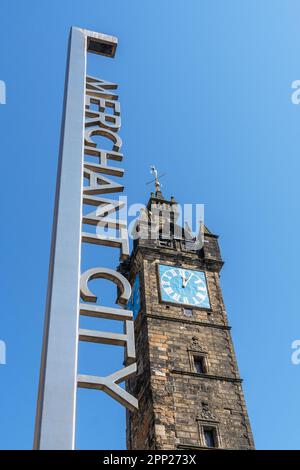 Schild für das Merchant City-Viertel von Glasgow, neben der historischen und mittelalterlichen Uhr in Glasgow Cross, Glasgow, Schottland, Großbritannien Stockfoto