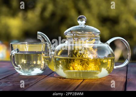 Schale mit Lindenblumen auf einem Holztisch im Garten. Leuchtend gelbe Blütenblätter und grüne Blätter sorgen für eine wunderschöne und natürliche Kulisse. Therapeutisch und medikamentös Stockfoto