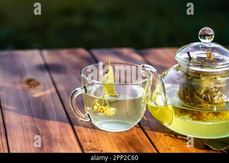 eine tasse heißen Lindentee mit Löffel und Lindenblumen auf einem Holztisch im Garten. Stockfoto