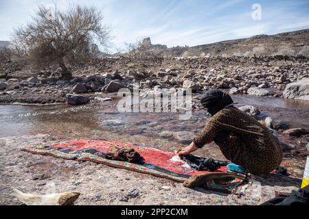 Berber-Frau wäscht Kleidung von Hand im Fluss mit den Zapfen von Babn Ali im Hintergrund. Stockfoto