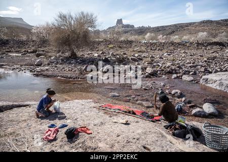 Berber-Frau wäscht Kleidung von Hand im Fluss mit den Zapfen von Babn Ali im Hintergrund. Stockfoto