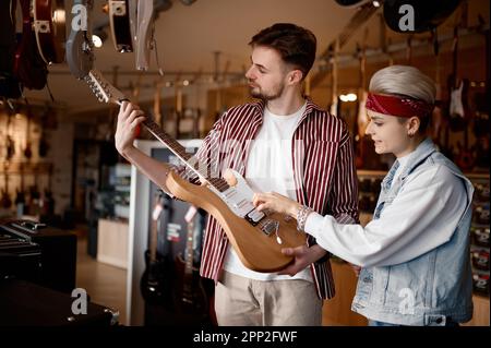 Ein junges Hipster-Paar, das nach einer neuen E-Gitarre für Auftritte sucht Stockfoto