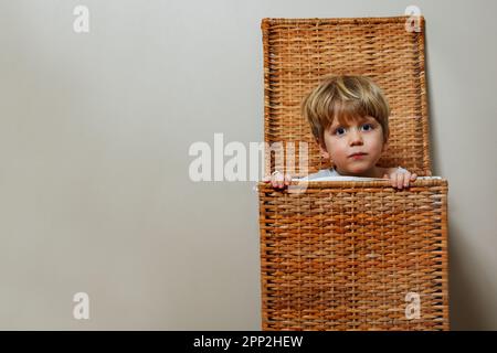 Nahporträt eines Jungen, der Verstecken in einer Wäschekiste spielt Stockfoto