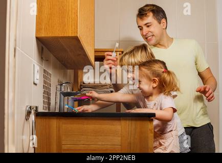 Dad mit zwei Kindern putzt Zähne mit einer Zahnbürste im Badezimmer Stockfoto