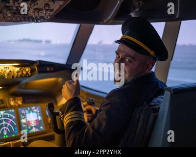 Kaukasischer bärtiger Mann, der beim Fahren eines Flugsimulators lächelt. Der Pilot im Cockpit zeigt Daumen nach oben. Stockfoto