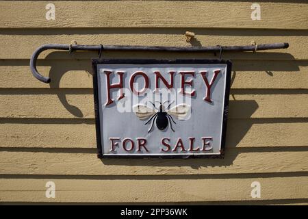 Haddam, Connecticut, USA: Gebäude mit Metallschild, auf dem „HONIG ZUM VERKAUF“ steht. Biene auf weißem Schild, das von einem alten Gehstock gehalten wird. Stockfoto