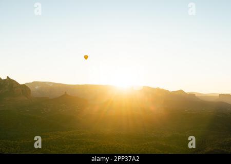 Breites Bild eines einzelnen Heißluftballons am Himmel, wenn die Sonne über den roten Felsen in Sedona Arizona aufgeht. Stockfoto