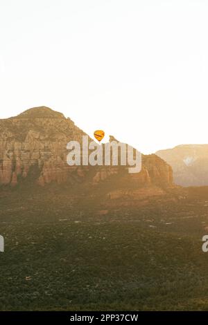 Der Heißluftballon erhebt sich während eines frühen Morgenflugs über den roten Felsberg. Stockfoto