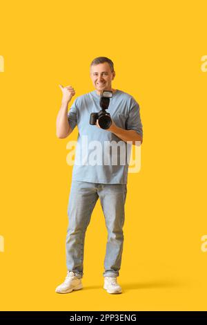 Reifer Fotograf mit professioneller Kamera, der auf etwas auf gelbem Hintergrund zeigt Stockfoto