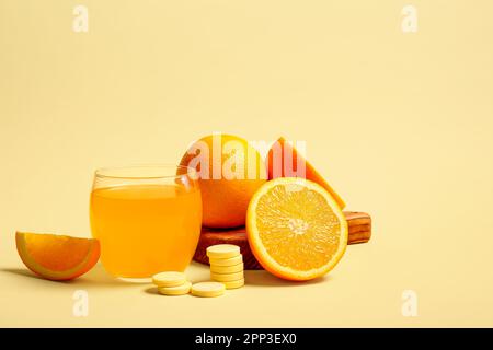 Brett mit Glas Vitamin-C-Brausetablette, gelöst in Wasser und Orangen auf beigefarbenem Hintergrund Stockfoto