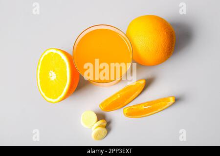 Glas Vitamin-C-Brausetablette, gelöst in Wasser und Orangen auf grauem Hintergrund Stockfoto