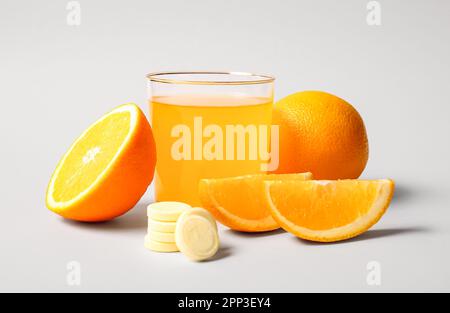 Glas Vitamin-C-Brausetablette, gelöst in Wasser und Orangen auf grauem Hintergrund Stockfoto