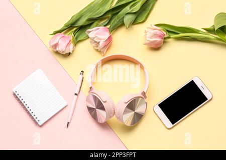 Moderne Kopfhörer, Mobiltelefon, Notebook und Tulpenblumen auf farbigem Hintergrund Stockfoto