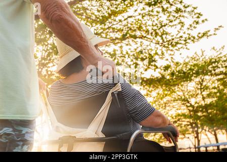 Seniorenpaar auf einem Spaziergang. Ein Mann trägt seine Frau im Rollstuhl Stockfoto