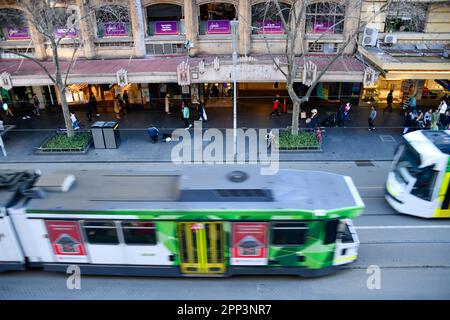 Die Straßenbahnen bewegen sich von oben auf der Bourke Street in Melbourne, während die Menschen auf dem Gehweg im Hintergrund auf dem Fußweg der Straße laufen Stockfoto