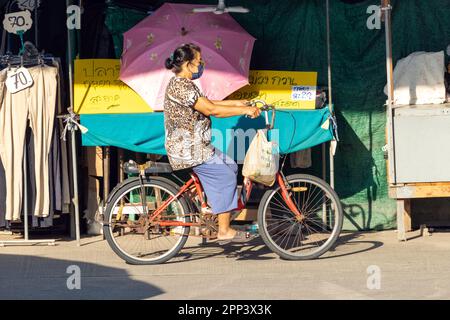 SAMUT PRAKAN, THAILAND, FEBRUAR 07 2023, Eine Frau fährt auf einem Fahrrad auf dem Marktplatz neben einem Stand Stockfoto