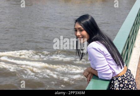 Eine junge Frau schaut von der Brücke über den Fluss Chao Phraya im Zentrum von Bangkok, Thailand Stockfoto