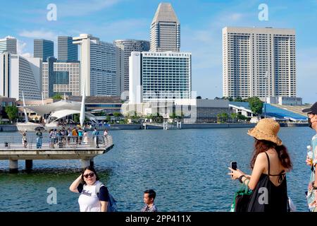 Ostasiatische Touristen genießen die Aussicht auf Marina Bay, Singapur, mit den verschiedenen Luxushotels und anderen Hochhäusern im Hintergrund Stockfoto
