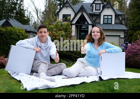 Junge Mädchen im Teenageralter sitzen mit Pizzaschachteln für Textnachrichten, Pizzeria und Fast Food Lieferrestaurant sitzen auf einem karierten Outdoor auf dem Gras zeigen Daumen-hoch-Anerkennung leckeres Essen, schöne Werbung Stockfoto