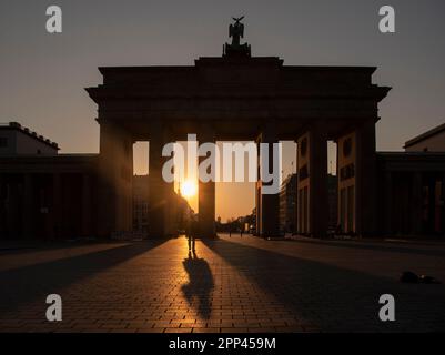 Berlin, Deutschland. 22. April 2023. Das Brandenburger Tor wirft Schatten in das Hintergrundlicht der aufgehenden Sonne. Kredit: Paul Zinken/dpa/Alamy Live News Stockfoto
