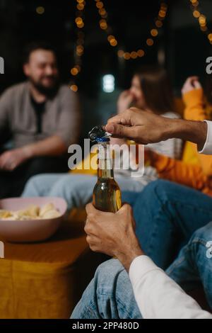 Eine Flasche Bier aus nächster Nähe öffnen. Eine Gruppe von Freunden hat Spaß beim Anschauen eines Films in einem Café. Stockfoto