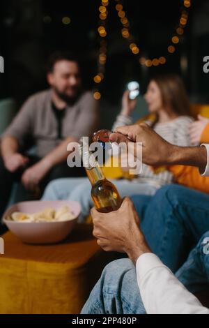 Eine Flasche Bier aus nächster Nähe öffnen. Eine Gruppe von Freunden hat Spaß beim Anschauen eines Films in einem Café. Stockfoto