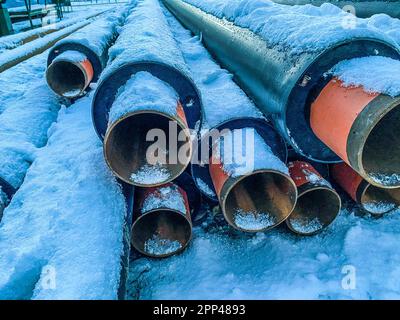 Lange, dünne, schwarze, schmale Rohre für die Verlegung von Leitungen. Polypropylenrohre sind in einem neuen Wohngebiet mit einer Schneeschicht bedeckt. TE Stockfoto