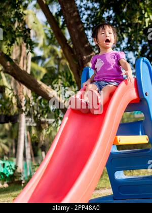 Fröhliches Kind, asiatisches Baby, das auf dem Spielplatz spielt, Slider Stockfoto