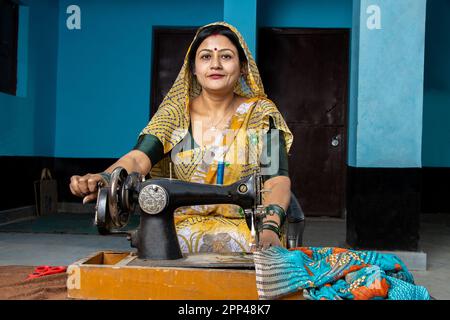 Porträt glückliche, traditionelle indische Hausfrau trägt Sari mit Nähmaschine zu Hause. Skill india-Konzept. Stockfoto