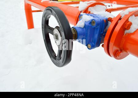 Industrielle Abschaltvorrichtungen zur Regelung von Schutzrohrfittings. Schwarzes Ventil zum Öffnen und Schließen eines orangefarbenen Metallrohrs mit Flanschen, Bolzen und Muttern Stockfoto