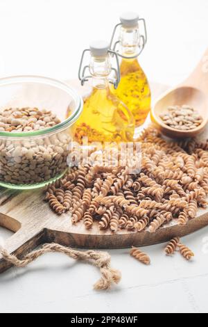 Grüne Fusilli-Nudeln mit Linsen auf grauem Betonhintergrund. Eine Schüssel mit roher Pasta und grünen Linsen. Glutenfreie Pasta. Stockfoto