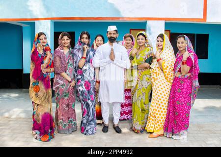 Ein indischer Politiker, der namaste mit einer Gruppe traditioneller Frauen macht. Konzept von Wahl und Abstimmung. Stockfoto