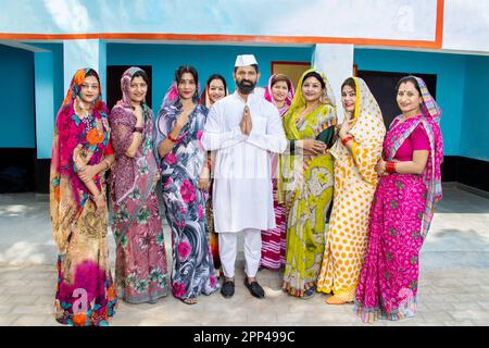 Ein indischer Politiker, der namaste mit einer Gruppe traditioneller Frauen macht. Konzept von Wahl und Abstimmung. Stockfoto