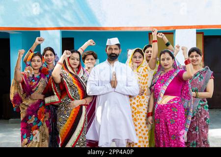 Ein indischer Politiker, der namaste mit einer Gruppe traditioneller Frauen macht. Konzept von Wahl und Abstimmung. Stockfoto