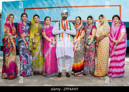 Ein indischer Politiker, der namaste mit einer Gruppe traditioneller Frauen macht. Konzept von Wahl und Abstimmung. Stockfoto