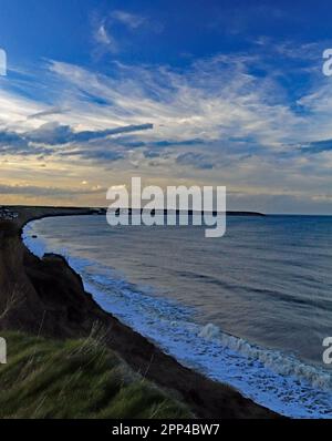 Hunmanby Bay an einem Frühlingsabend unter einem großen blauen Himmel mit weißen Wolken, die mit Gezeiten und dem Meer, das gegen die Felsenböden spritzt. Stockfoto
