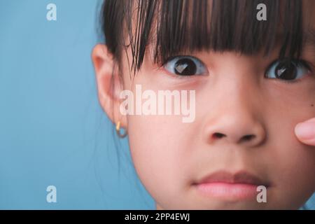 Nahaufnahme eines überraschten jungen Asiaten auf blauem Hintergrund. Ein süßes, schockiertes Mädchen mit großen schwarzen Augen reagiert überraschend auf etwas Stockfoto