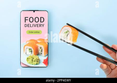 Sushi-Set über die Mobiltelefon-App bestellen. Konzept der Online-Lebensmittellieferung. Bestellen Sie eine Mahlzeit in einem Restaurant über die App auf Ihrem Mobiltelefon. Stockfoto