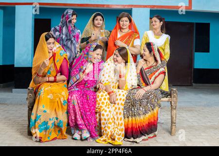 Eine Gruppe glücklicher junger, traditioneller indischer Frauen, die farbenfrohe Sari tragen, lachen, sich unterhalten und Spaß miteinander haben. Ländlicher Haushalt. Stockfoto