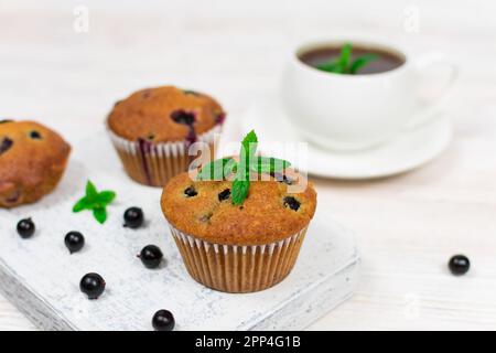 Cupcakes mit schwarzer Johannisbeere und Minzblättern auf einem weißen Teller mit einer Tasse Tee. Selektiver Fokus. Stockfoto