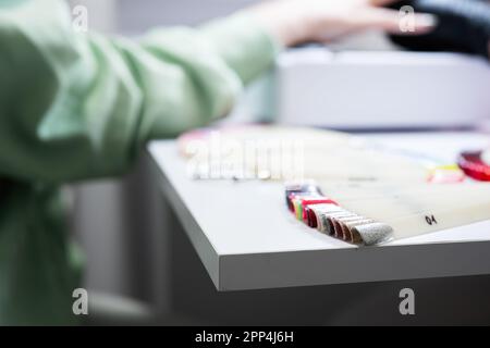 Manikürmeister arbeitet mit weiblicher Klientin im Schönheitssalon. Die Frau wählt die Farbe des Nagellacks aus der Palette. Stockfoto