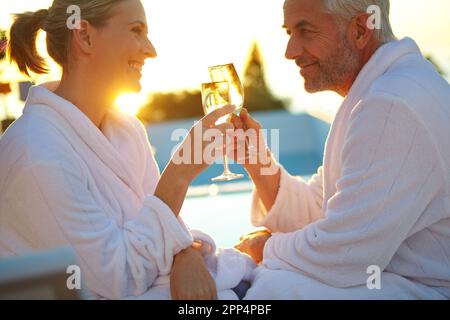Feiert ihr Jubiläum mit Stil. Ein reifes Paar, das Champagner trank, während es sich bei Sonnenuntergang auf den Liegestühlen entspannte. Stockfoto
