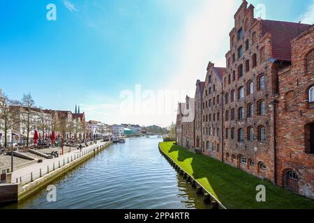 Lübeck, Deutschland, 17. April 2023: Historische Salzlagergebäude und Promenade mit Cafés am Ufer des Flusses Trave in der Altstadt von Lübeck, to Stockfoto