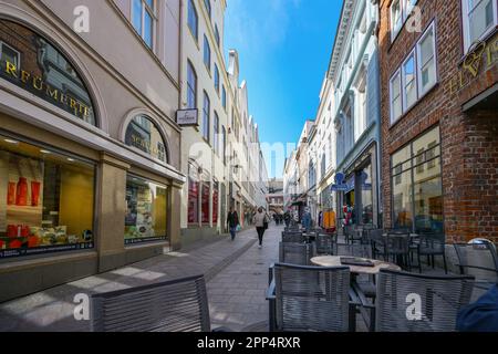 Lübeck, Deutschland, 17. April 2023: Schmale Fußgängerzone mit Geschäften und Straßencafés in der historischen Altstadt der hansestadt Lübeck, selecte Stockfoto