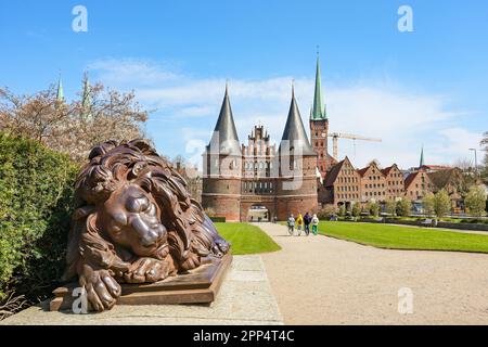 Eine schlafende Löwenskulptur aus Eisen vor dem Lubeck Holstentor oder Holsten Gate, ein historisches Wahrzeichen und Touristenziel unter einem blauen Skay, Symb Stockfoto