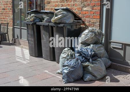 Überfüllte Mülltonnen und Müllsäcke voller Müll auf dem Bürgersteig in der Stadt, tägliche Müllproduktion der Wohlstandsgesellschaft, ausgewählter Fokus Stockfoto