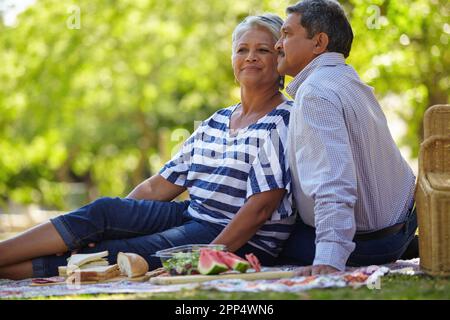 Es gibt nichts Romantischeres als ein Picknick. Ein liebevolles Seniorenpaar, das ein gemütliches Picknick im Park genießt. Stockfoto