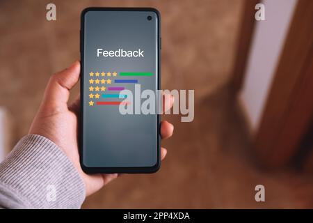Eine Frau hält ein Smartphone mit einer Benutzeroberfläche für Kundenbewertungen auf dem Bildschirm. Bewertungsservice. Online-Anwendung für Kundenzufriedenheit. Stockfoto