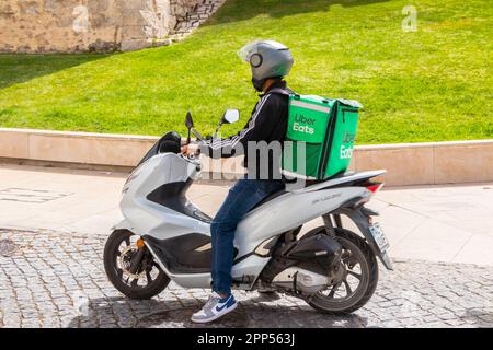 Ein junger Mann auf einem Moped-Roller, der für Uber liefert, isst in loule portugal Lebensmittel Stockfoto